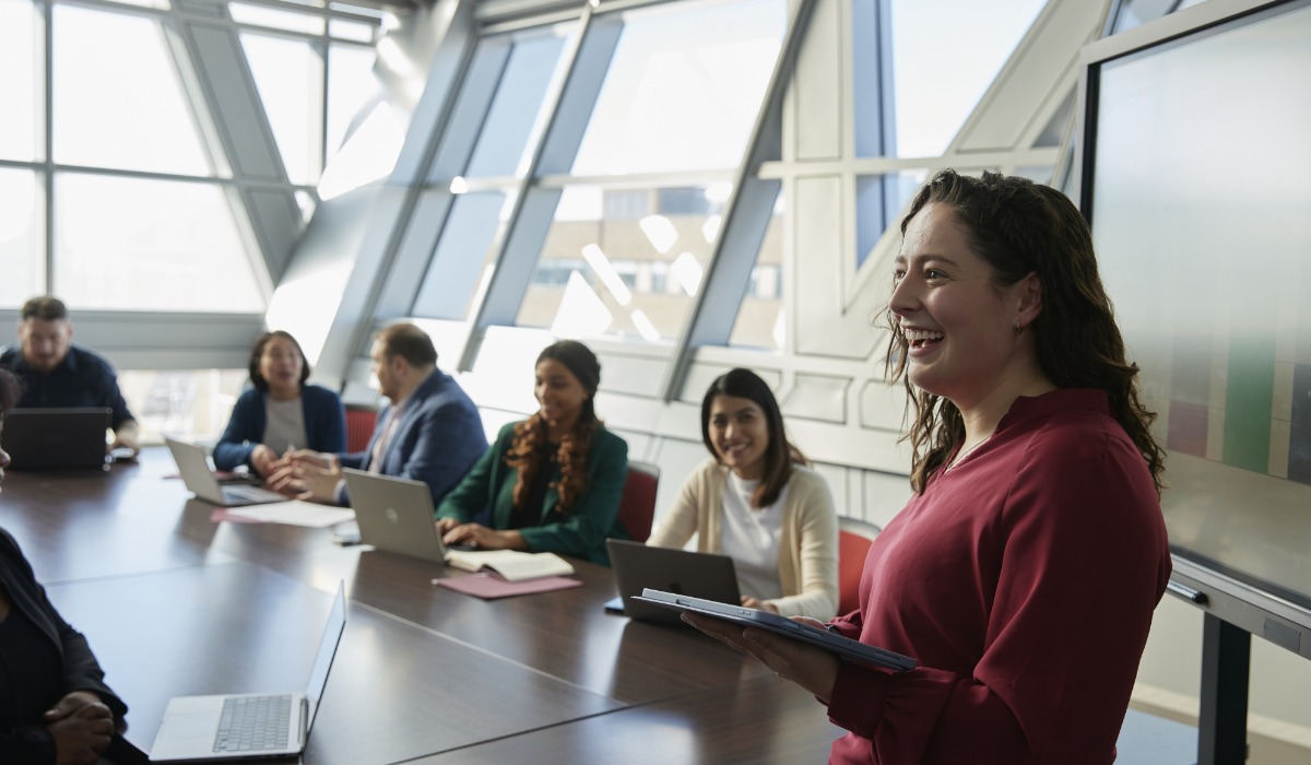 A professional woman presents confidently in a modern conference room filled with engaged colleagues.