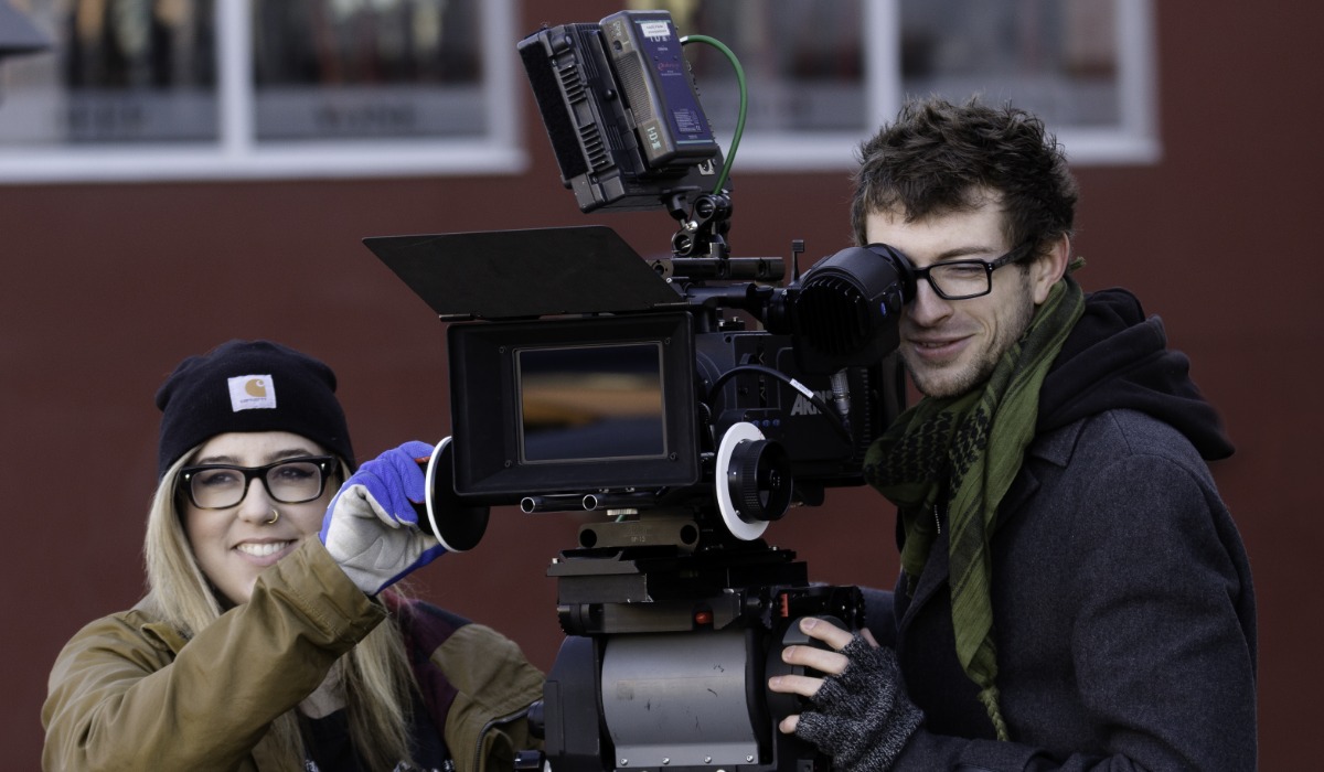 A filmmaker and a technician working together on a camera setup outdoors.