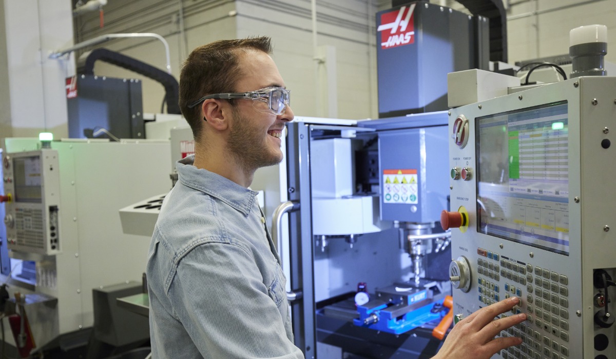 A technician operating a CNC machine, focusing on the control panel and programming process in a modern manufacturing setting.