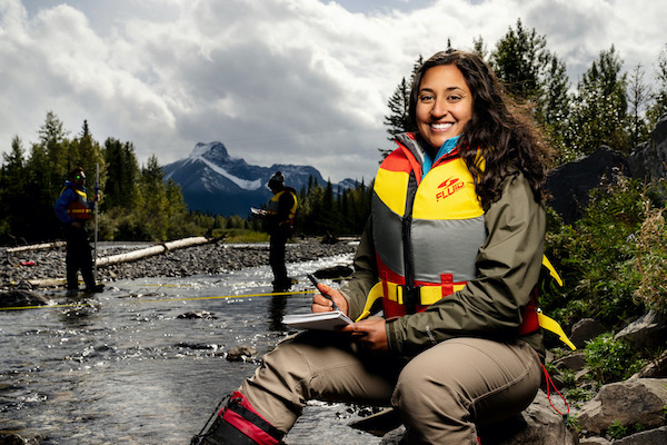 An Environmental Technology students sits beside a river wearing a lifejacket.